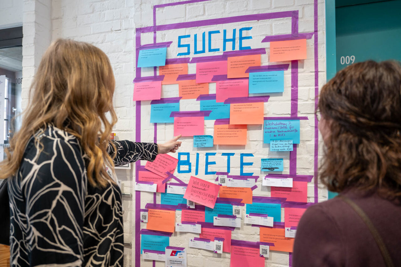 Das Bild zeigt eine Aufnahme von Menschen vor der Suche-Biete-Wand von 4transfer während der Townhall Saxony 2026