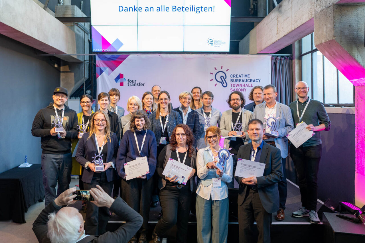 Das Bild zeigt die Protagonist:innen der zehn Projekte, die sich. bei der Creative Bureaucracy Townhall Saxony am 26. März 2026 in Dresden präsentiert haben. Außerdem zu sehen die mehrere Mitglieder der Jury, die die Projekte im Vorfeld ausgewählt haben.